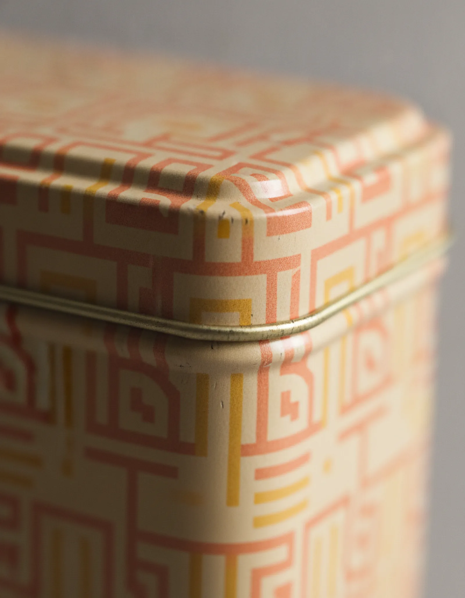Close-up of an embossed pattern on a cream and coral tin lid, raised metal edges catching light