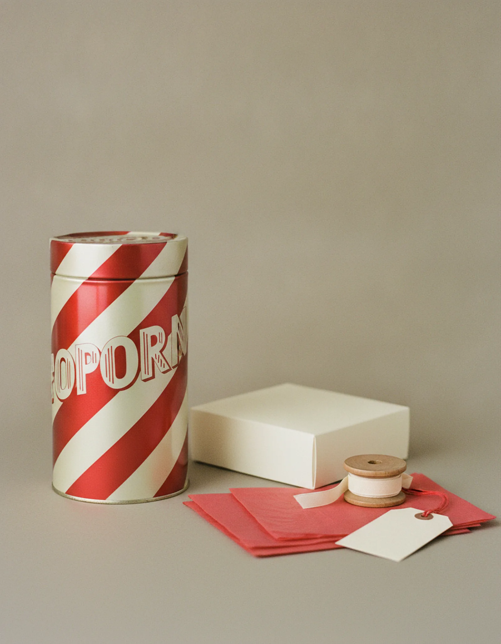Large vintage-style popcorn tin beside a flattened stack of gift boxes, tissue, and ribbon spools