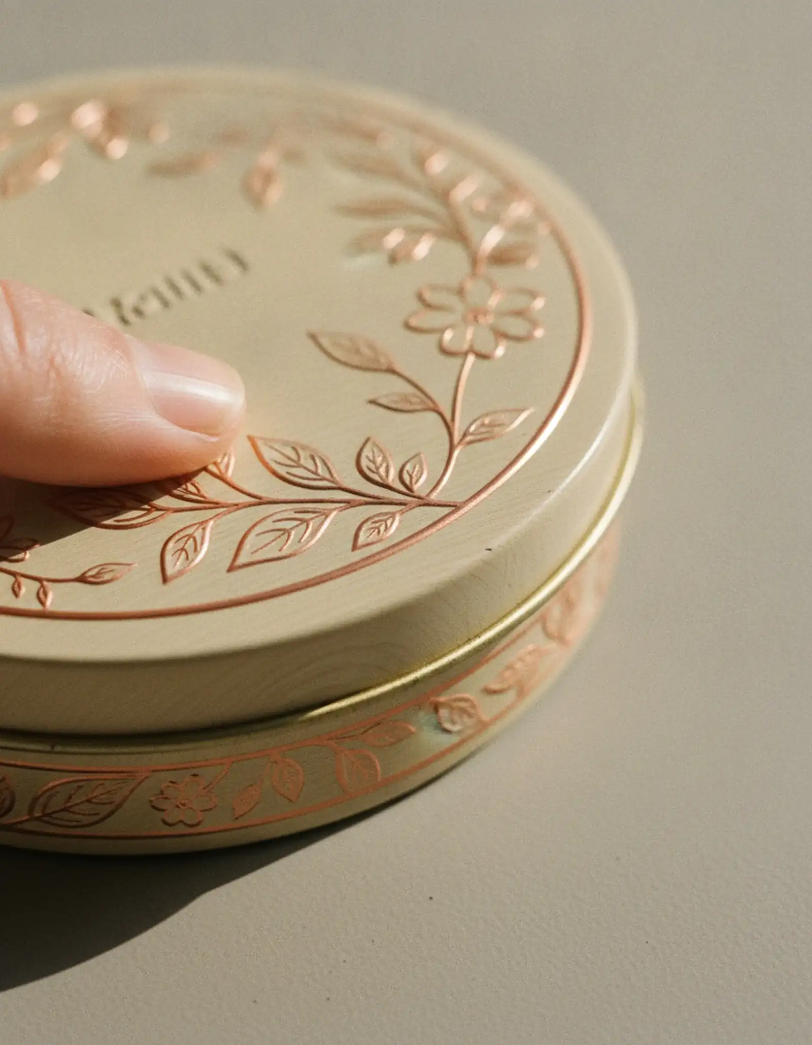 Close-up of an embossed cream and copper tin lid showing raised botanical detail