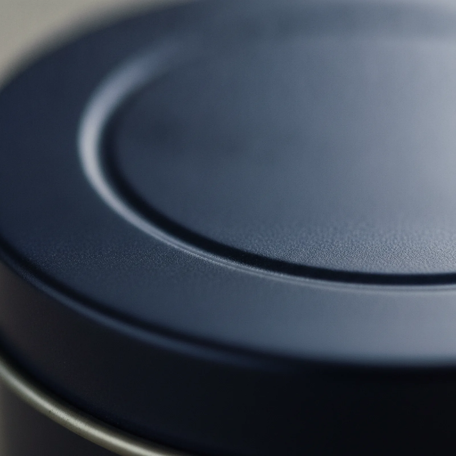 Macro close-up of a logo debossed into a matte navy tin lid