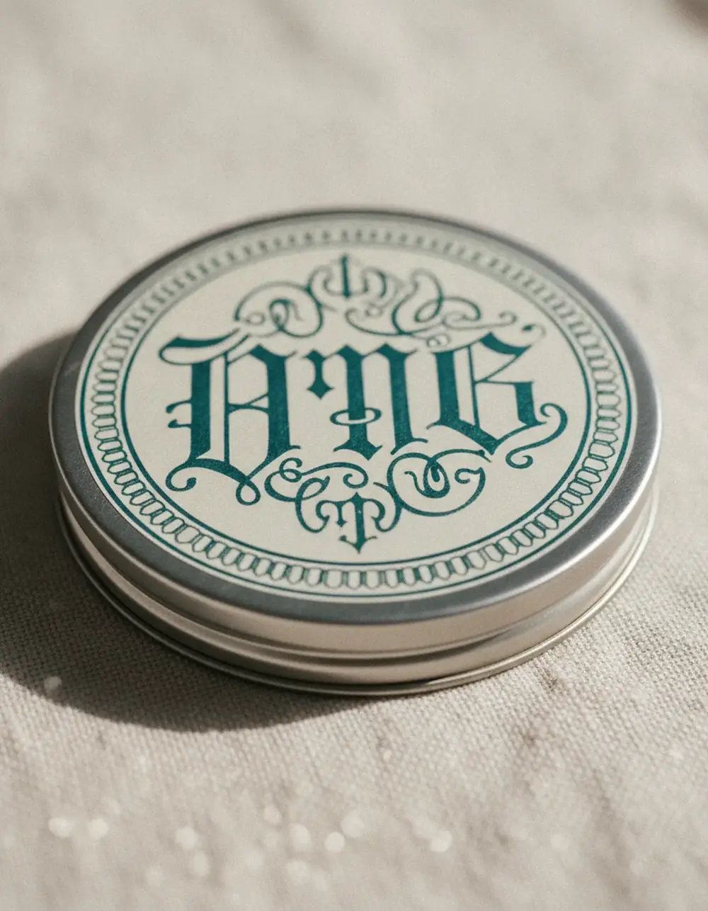 Close-up of an ornate hand-lettered teal monogram on a round tin lid with a decorative border
