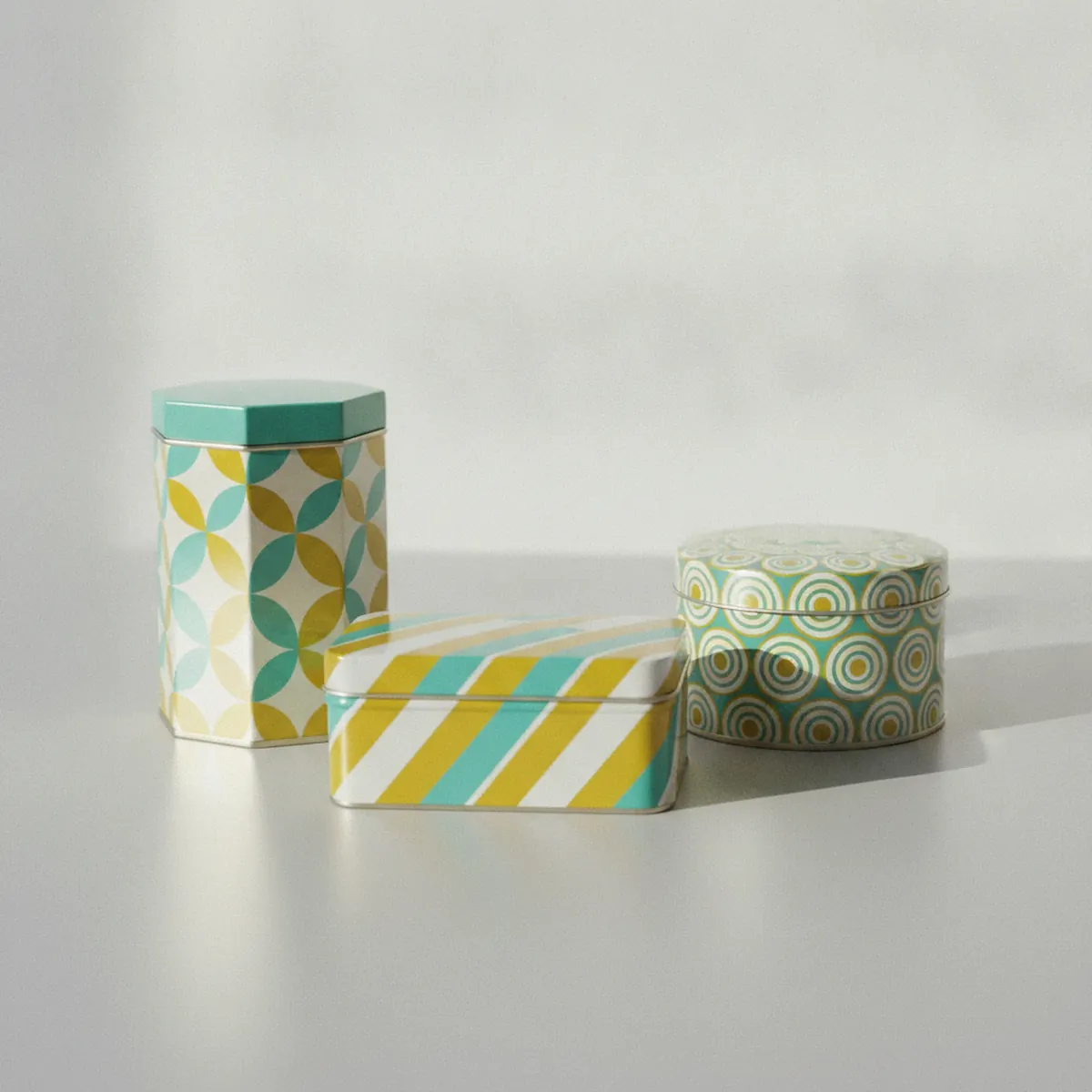Three differently shaped decorative tins in a mid-century colour palette on a pale surface