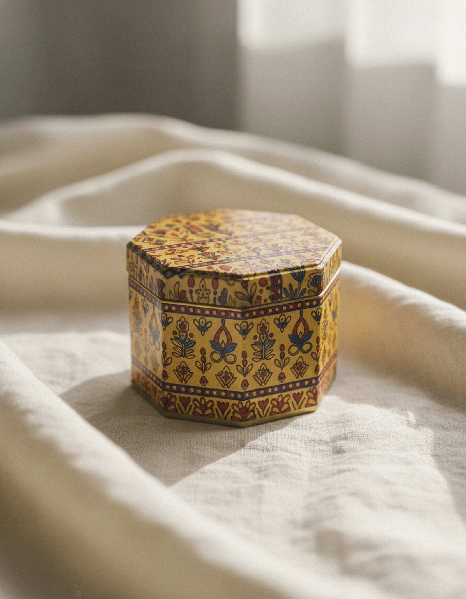 Hexagonal decorative tin with hand-drawn botanical and geometric motifs on a folded linen textile
