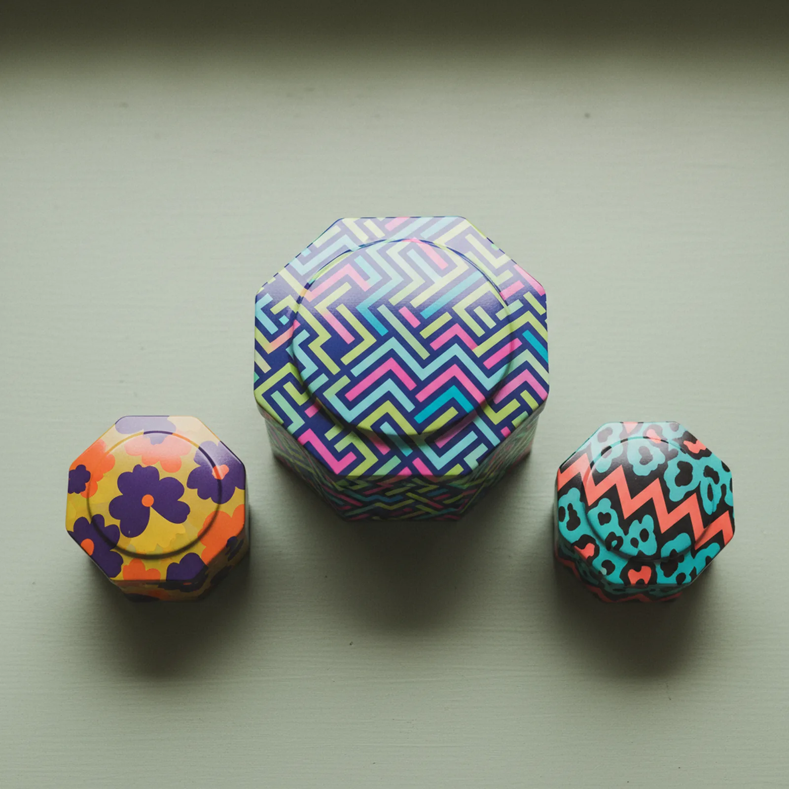 Three specialty-shape tins — octagonal, pillow, and star — on a pale sage green wood surface